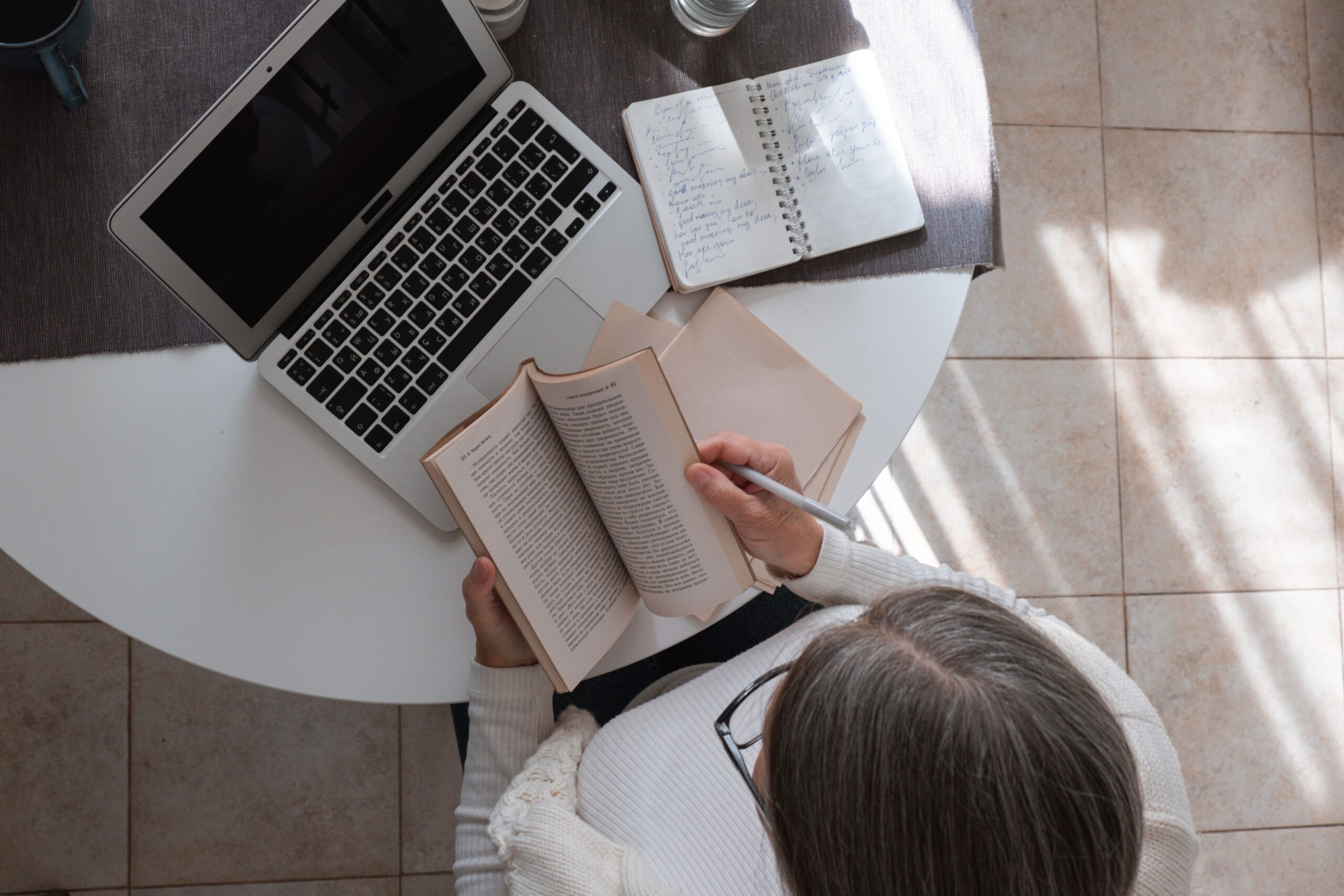 Overhead view of a woman studying with a laptop and open book on a table, creating a productive atmosphere.